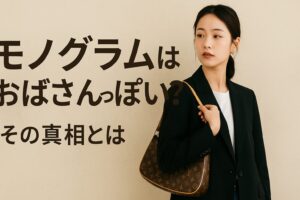 代替テキスト:黒のジャケットを着た若い女性がベージュの背景の前でルイヴィトンのモノグラムバッグを肩にかけ、「モノグラムはおばさんっぽい?その真相とは」という日本語テキストと共にスタイリッシュな雰囲気でポーズをとっている。